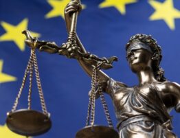 Estatua de la diosa de la justicia vendada, Themis o Justicia, frente a una bandera europea, como un concepto legal.