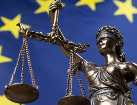 Estatua de la diosa de la justicia vendada, Themis o Justicia, frente a una bandera europea, como un concepto legal.